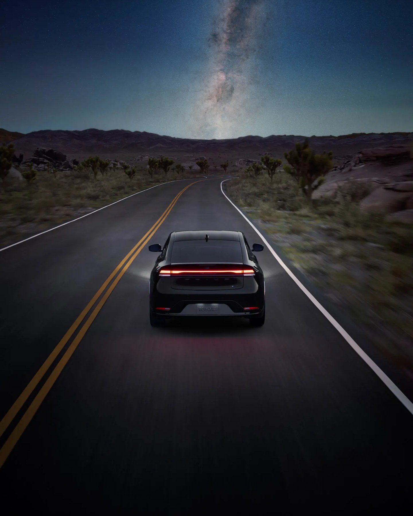 Black Toyota electric SUV driving on a desert road under a starry night sky with the Milky Way visible.