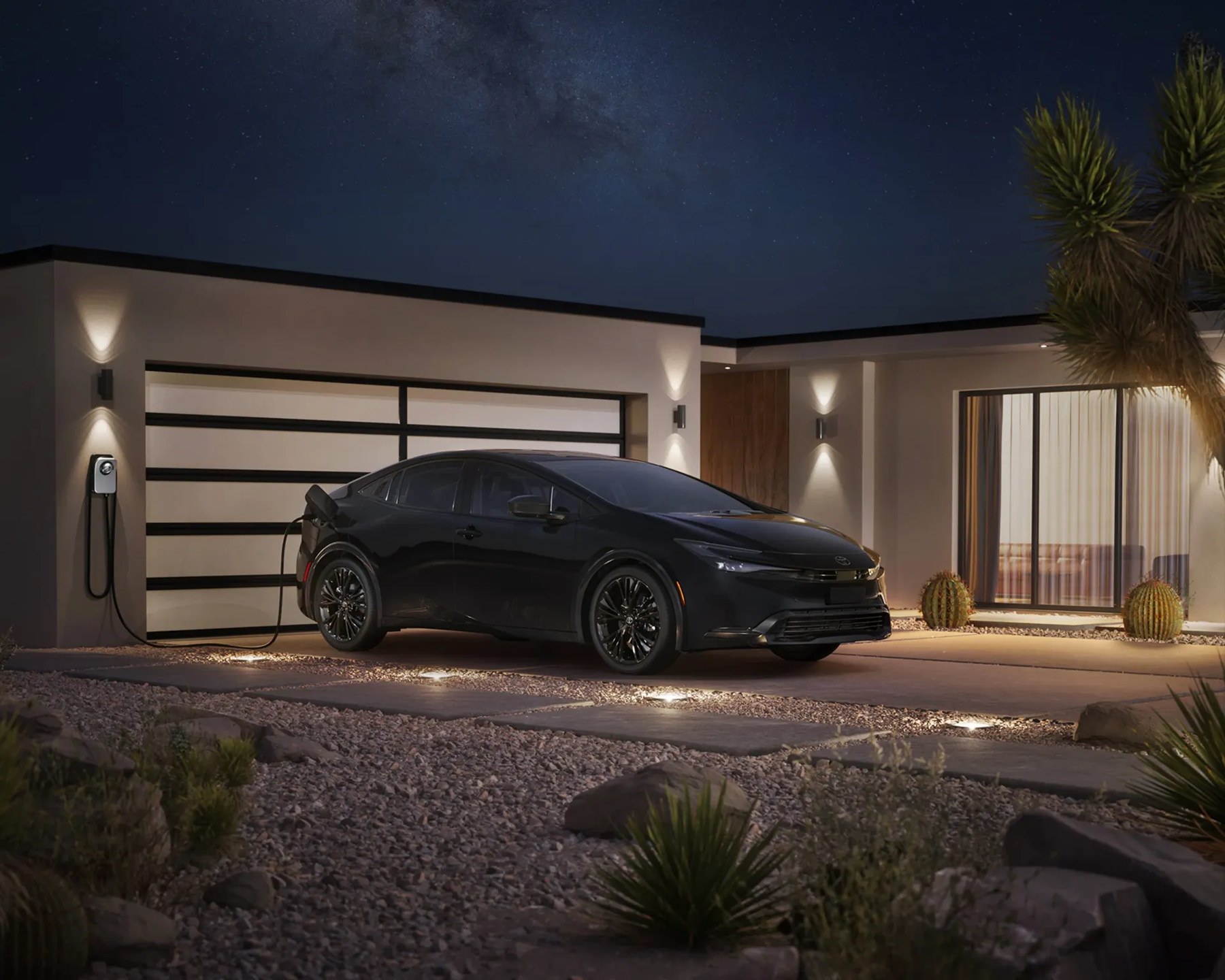 Black electric sedan plugged into a wall charger outside a modern house at night.